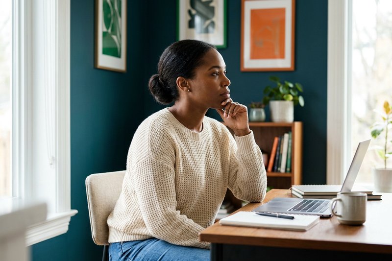 Solopreneur sitting thoughtfully at a home office desk with a laptop and coffee, reflecting on the emotional ups and downs of running a business alone